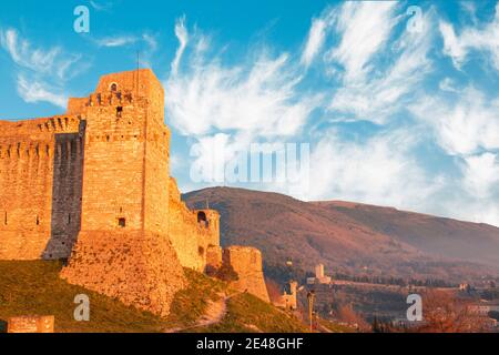 Vue rapprochée du château médiéval en haut de la colline d'Assise, province d'Ombrie Italie. Tour de briques en pierre et murs au coucher du soleil avec des nuages clairs ciel et Banque D'Images