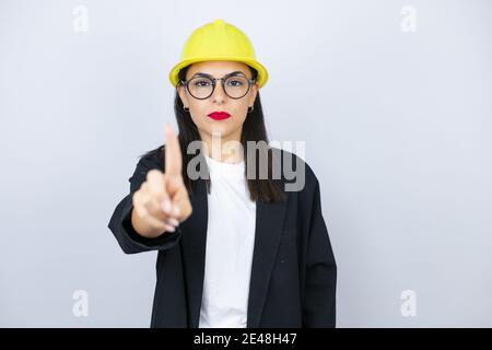 Jeune architecte femme portant un casque résistant montrant et pointant avec les doigts numéro un alors que est grave Banque D'Images