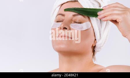 Une photo agrandie d'une femme âgée avec une peau équitable, des taches cosmétiques pour les yeux et une feuille d'aloe vera. Arrière-plan blanc. Banque D'Images