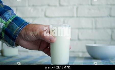 Une personne prend et boit un verre avec du lait frais au petit déjeuner une boisson saine, savoureuse et naturelle pleine de protéines et de vitamines Banque D'Images