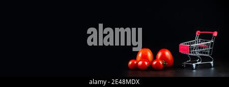 Prise de tomates mûres savoureuses dans un panier ou un chariot sur fond blanc. Concept de commerce de tomates. Concept d'achat en ligne. Taille de la bannière. Copier l'espace. Banque D'Images