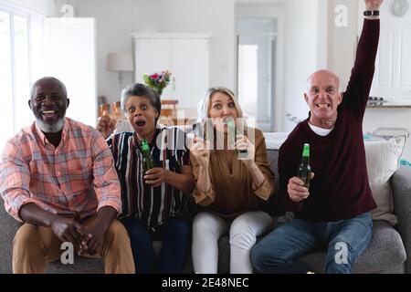 Couples de personnes âgées de race blanche et afro-américaine assis devant un canapé bière de gibier à la maison Banque D'Images