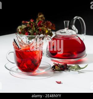 Infuse de tisane rouge dans une tasse avec théière transparente, aubépine, baie de rosehip, feuilles séchées dans un intérieur noir et blanc contrasté, carré. Banque D'Images