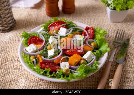 Salade chaude avec potiron, fromage feta, tomates séchées, olives, arugula et oignon rouge. Gros plan. Banque D'Images