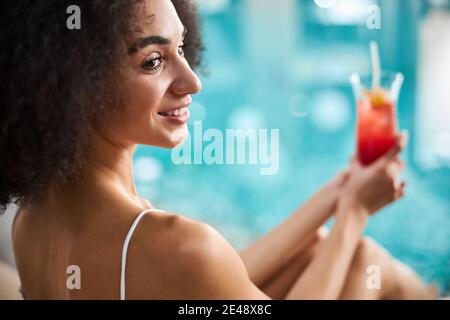 Une dame afro-américaine décontractée qui a un délicieux cocktail près de la piscine Banque D'Images