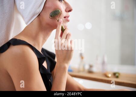 Jeune femme concentrée utilisant le rouleau pour traiter sa peau de visage Banque D'Images