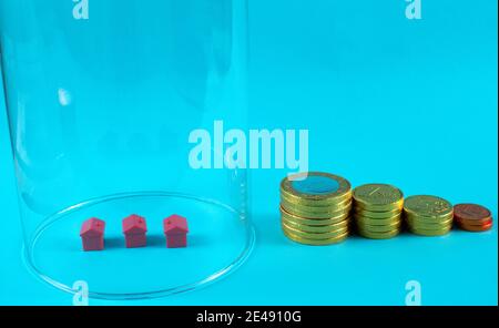 Maisons miniatures à l'intérieur d'un verre avec des pièces empilées sur le dessus de chacun sur fond bleu Banque D'Images