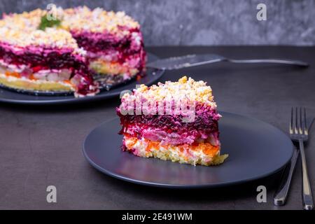 Salade de hareng sous un manteau de fourrure. Salade russe traditionnelle composée de plusieurs couches de hareng, de betteraves, de pommes de terre, de carottes et d'œufs. Gros plan, fond gris. Banque D'Images