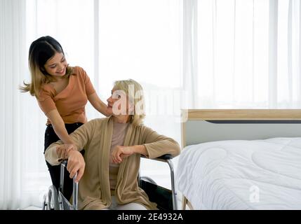 Happy MIX peau famille vivant ensemble, fille asiatique prend soin de sa mère caucasienne adoptée assise sur un fauteuil roulant. Concept d'amour et de partage Banque D'Images