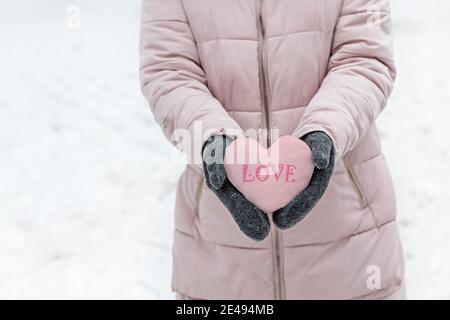 Les mains des femmes sont en moufles grises chaudes avec un coeur rose enneigé. Le concept de la Saint-Valentin. L'inscription sur l'amour du coeur . Banque D'Images