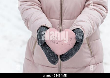 Les mains des femmes sont en moufles grises chaudes avec un coeur rose enneigé. Le concept de la Saint-Valentin. L'inscription sur l'amour du coeur . Banque D'Images