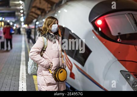 Une jeune femme dans un masque médical se tient sur la plate-forme de la gare, attendant le départ d'un train à grande vitesse. La pandémie du coronavirus Banque D'Images