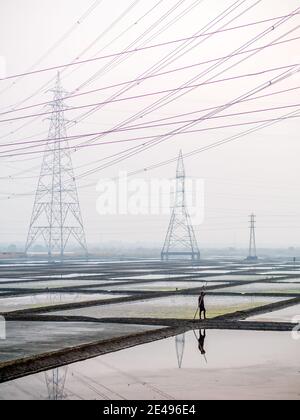 MUMBAI, INDE - 17 décembre 2020 : ouvriers non identifiés dans une ferme de sel de mer et une grange avec des lignes électriques haute tension en arrière-plan Banque D'Images