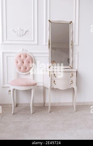 chambre classique avec mur blanc à motifs, coiffeuse avec miroir, chaise douce dorée et rose. Détails de l'intérieur de la chambre Banque D'Images