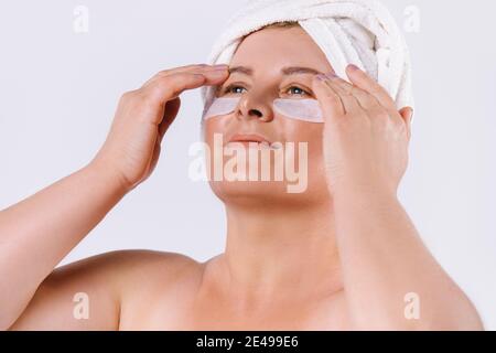 Une photo agrandie d'une femme âgée à la peau équitable avec une serviette blanche sur sa tête et des taches sous ses yeux regardant sur un fond blanc Banque D'Images