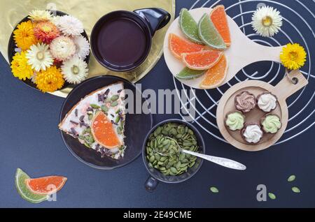 Un morceau de gâteau avec du café, des bonbons, des graines de citrouille et des fleurs sur un fond sombre. Mise au point sélective, vue de dessus Banque D'Images