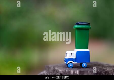 Camion à ordures jouet avec un poubelle verte peut se tenir sur un arbre de chanvre contre un fond de forêt flou. Mise au point sélective, espace de copie. Forêt propre conc Banque D'Images