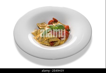 raviolis avec sauce tomate et tranches de tomates cerises et feuilles de basilic en plaque blanche isolées sur fond blanc Banque D'Images