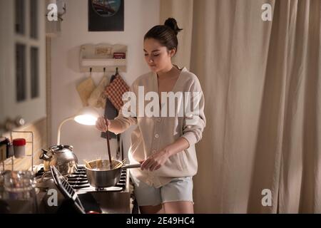 Jeune femme remuant les pâtes dans une casserole tout en regardant la recette en ligne à la maison Banque D'Images