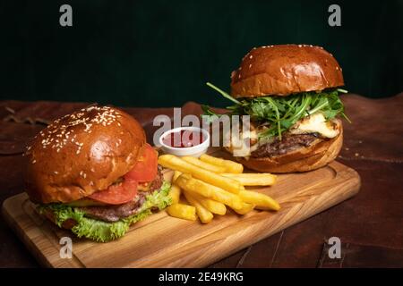 Des hamburgers de bœuf américains frais et délicieux servis avec des frites, un avec des noix frites et du fromage grillé sur une partie décorative en bois de simple Banque D'Images