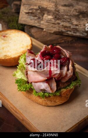 Hamburger artisanal créatif démonté avec tranches de bacon frites et sauce aigre-douce et cerise sur le dessus, laitue fraîche avec pain de plomb à côté Banque D'Images