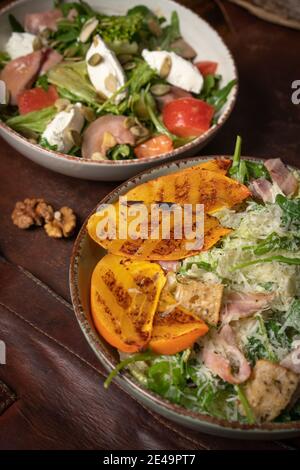 Deux bols de salades avec du saumon, de la mozzarella et des tranches de fruits grillées se dressent sur une table recouverte d'un chiffon en cuir. Concept de restaurant Banque D'Images