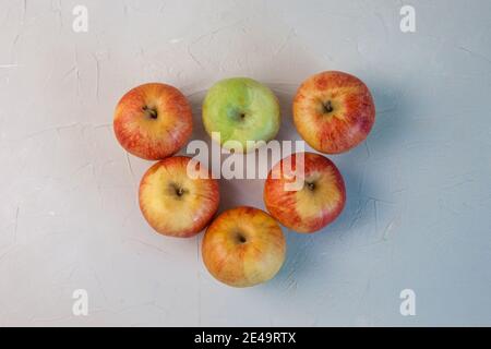 Cinq pommes rouges et une pomme verte sont en forme de triangle sur fond gris. Gros plan Banque D'Images