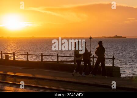 Femelles sur la promenade du front de mer à Southend on Sea au lever du soleil. Promenade tôt le matin à l'aube froide de l'hiver. Enveloppé de vêtements chauds et prenant des selfies Banque D'Images