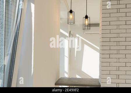 Deux lampes en acier éclairent une table de bar contre un mur dans un style moderne minimaliste avec une couleur blanche le mur au-dessus du comptoir et marron en dessous Banque D'Images