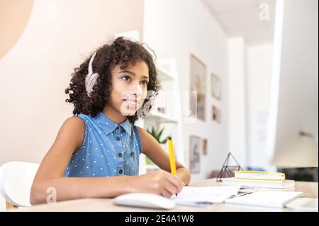 Smart petite fille africaine remplir dans le livre d'exercice, regarder des cours vidéo, la formation pour un examen, la recherche de sujet pour essai, étudier à distance, faire des devoirs. Étude et technologie Banque D'Images