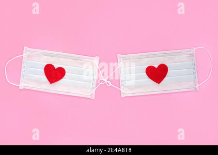 Deux masques médicaux attachés sur fond rose avec des coeurs rouges en feutre sur eux comme symbole de l'unité de l'amour pendant les virus. Banque D'Images