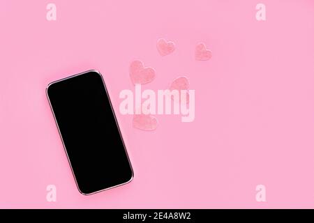 Modèle de téléphone avec écran noir avec coeur en feutre sur fond rose. Copier l'espace. Conversation en ligne, anniversaire ou Saint-Valentin. Banque D'Images