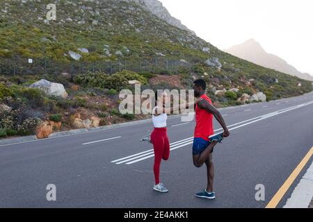 S'adapte à un couple afro-américain dans des vêtements de sport s'étendant sur une côte route Banque D'Images