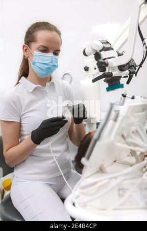 Portrait vertical d'un dentiste professionnel portant un masque médical, utilisant un équipement dentaire moderne Banque D'Images