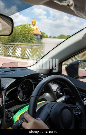 Conduire une voiture sur la route en Thaïlande. Vue sur une statue de Bouddha à travers le pare-brise d'une voiture en mouvement. Banque D'Images