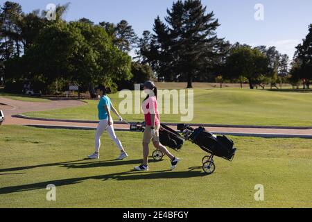 Deux femmes de race blanche marchant sur le parcours de golf tirant des sacs de golf sur roues Banque D'Images