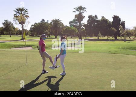 Deux femmes caucasiennes portant des masques saluant sur le terrain de golf en touchant les chevilles Banque D'Images