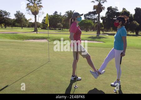 Deux femmes caucasiennes portant des masques saluant sur le terrain de golf en touchant les chevilles Banque D'Images