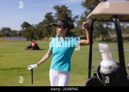 Femme caucasienne jouant au golf en se penchant sur la voiturette de golf au golf cours Banque D'Images