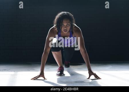 Femme afro-américaine portant des vêtements de sport à genoux en train de courir dans un bâtiment urbain vide Banque D'Images