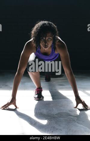 Femme afro-américaine portant des vêtements de sport à genoux en train de courir dans un bâtiment urbain vide Banque D'Images