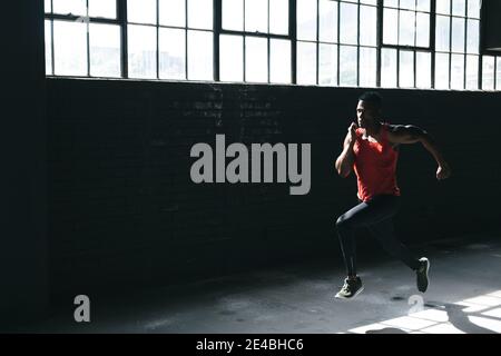 Homme afro-américain portant des vêtements de sport sprinting dans les villes vides bâtiment Banque D'Images