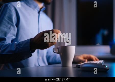 Vue latérale des mains d'un homme méconnaissable qui verse du sucre sur le café dans une tasse avec une petite cuillère en métal Banque D'Images