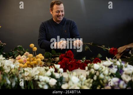 Fleuriste caucasien vendant des bouquets de roses rouges et roses pour la Saint-Valentin. Concept des émotions humaines, de l'expression faciale, de l'amour et du travail acharné Banque D'Images