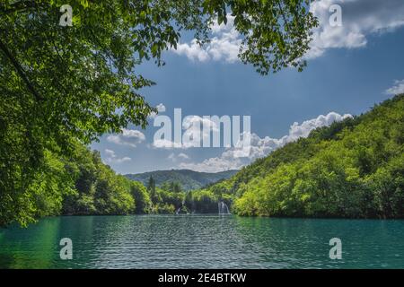 Lac turquoise et cascades illuminées par la lumière du soleil encadrées par des branches dans une forêt luxuriante, Parc national des lacs de Plitvice patrimoine mondial de l'UNESCO, Croatie Banque D'Images