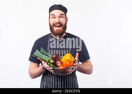 Photo d'un jeune chef émerveillé en uniforme tenant quelques légumes frais. Banque D'Images