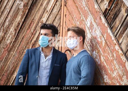 Groupe de jeunes, temps libre dans la ville. Debout à l'extérieur. Deux personnes se rencontrent, sans distance, en portant un masque dans l'espace public. Exigence de masque. Banque D'Images