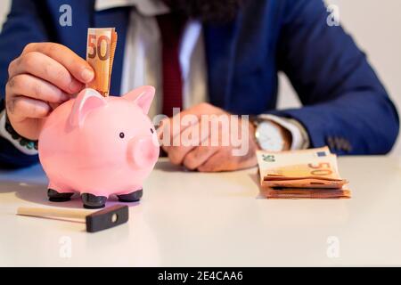 Homme d'affaires mettant cinquante euros d'argent de billet de banque dans la piggy banque. Concept financier et économique Banque D'Images
