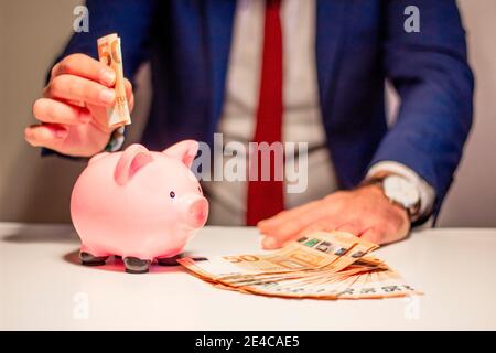 Homme d'affaires mettant cinquante euros d'argent de billet de banque dans la piggy banque. Concept financier et économique Banque D'Images
