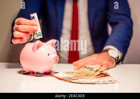 Homme d'affaires mettant cinquante euros d'argent de billet de banque dans la piggy banque. Concept financier et économique Banque D'Images